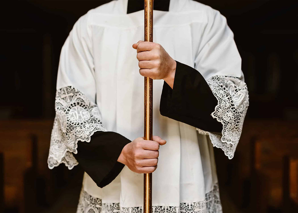 An altar server in a white alb holding a golden cross against a dark background.